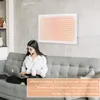 A woman is sitting on a couch using a laptop, with a wall heater on the wall behind her. Náhled obrázku produktu