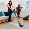 A woman is vacuuming a rug in a living room with a cordless vacuum cleaner. Náhled obrázku produktu