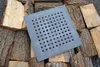 A square metal grate with many holes is placed on a pile of chopped wood. Produktbild-Vorschau