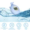 A light blue whale-shaped bath thermometer floating in water, with icons and text below. Produktbild-Vorschau