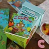A collection of children's books and a box set, with gummy candies and a wooden letter 'C' on a wooden surface. Produktbild-Vorschau