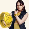 A woman wearing a yellow smartwatch and jewelry, with a close-up of the smartwatch in the foreground. Voir les images du produit
