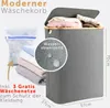 A modern gray laundry basket with a lid, filled with clothes. Next to it are folded clothes and a mesh laundry bag. Dimensions are indicated. Produktbild-Vorschau