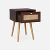 A dark wood effect nightstand with a rattan drawer front and wooden legs, shown against a white background. Produktbild-Vorschau