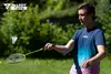 A man playing badminton outdoors in a grassy area with trees in the background. Produktbild-Vorschau