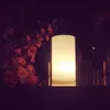 A lit lamp is placed next to a bouquet of flowers in a dimly lit setting. Produktbild-Vorschau