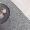 A close-up view of a grey rug next to a wooden floor, with a grey coffee table holding two small vases. Produktbild-Vorschau