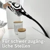 A hand holding a cordless vacuum cleaner with a long nozzle, positioned to clean a hard-to-reach area next to two decorative jars on a white surface. The text "Für schwer zugängliche Stellen" (For hard-to-reach places) is overlaid on the image. Produktbild-Vorschau