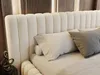 A close-up view of a bed with a beige upholstered headboard and pillows. Produktbild-Vorschau