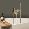 A modern bathroom scene with a gold bathtub faucet and showerhead, a wooden bath tray with a soap dispenser and candle, and a white bathtub. Podgląd zdjęcia produktu