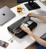 A person is organizing accessories inside a laptop bag on a desk. Náhľad obrázku produktu