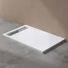 A white rectangular shower tray with a silver drain is shown on a concrete floor against a brown wall. Produktbild-Vorschau