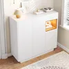 A white shoe cabinet with a natural wood accent is shown in a modern entryway, with decorative items on top and a rug in front. Produktbild-Vorschau