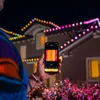 A person is holding a smartphone displaying a light pattern, while controlling a string of colorful LED lights on the exterior of a house at night. Náhled obrázku produktu