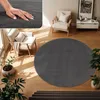 A round gray rug is placed on a wooden floor in a living room setting, with a chair and plants nearby. Produktbild-Vorschau
