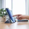 A hand is shown touching the screen of a tablet in a case, with a plant and books in the background. Voir les images du produit