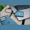 A blue Verbatim SnapBack SSD is connected to a laptop, with a blue iPhone in the foreground, all resting on a wooden surface. Náhľad obrázku produktu