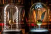 Two Harry Potter Golden Snitch replicas displayed under glass domes, with a bookshelf background. Podgląd zdjęcia produktu