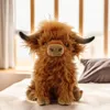A plush toy Highland cow sits on a bed in front of a window. Produktbild-Vorschau