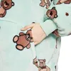 Hellgrüne Fleece-Loungewear mit braunem Teddybär-Motiv, eine Hand in der Vordertasche Produktbild-Vorschau