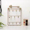 A gold-colored key-shaped jewelry organizer with multiple hooks is displayed against a white background. Two lipsticks are placed to the right of the organizer. Náhľad obrázku produktu