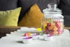A glass jar filled with colorful gummy candies sits on a table next to three lit tea lights. Podgląd zdjęcia produktu