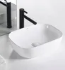 A white ceramic washbasin with a black faucet is shown on a white surface, with a mirror reflecting another faucet in the background. Produktbild-Vorschau