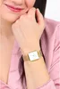 A woman's wrist wearing a gold square watch with a white face. Podgląd zdjęcia produktu