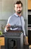 A man is standing in a kitchen, opening the lid of a coffee machine. Voir les images du produit
