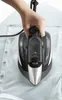 A hand is holding a steam iron and ironing a light blue shirt. Produktbild-Vorschau