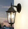 An outdoor wall light mounted on a white wall, with a twilight sky and house in the background. Produktbild-Vorschau