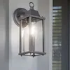 An outdoor wall lamp is mounted on a white wall next to a window with blinds. Voir les images du produit