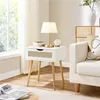 A white nightstand with a rattan drawer front is placed next to a sofa in a well-lit room. Podgląd zdjęcia produktu