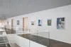 A modern interior hallway with paintings displayed on the wall and a glass railing. Voir les images du produit