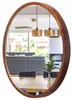 A round wooden mirror reflects a dining area with chairs and a table, and a living room with a sofa and fireplace. Produktbild-Vorschau