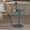 A teal side table with a vase and cup on it, next to a wicker chair. Produktbild-Vorschau