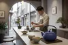 A man preparing tea in a tea shop with a blue teapot and cups on the counter. Podgląd zdjęcia produktu