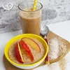 A bowl of oatmeal topped with apple slices and a glass of smoothie with a straw, set against a brick wall. Produktbild-Vorschau