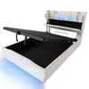 A white upholstered bed frame with the hydraulic storage mechanism open, revealing the black storage compartment. The headboard has built-in shelving with blue LED lighting. Náhľad obrázku produktu