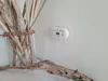 A white carbon monoxide detector is mounted on a light gray wall, next to a vase filled with driftwood. Podgląd zdjęcia produktu