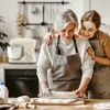 Two women, one older and one younger, are in a kitchen preparing dough. The younger woman has her arm around the older woman's shoulders, and they are both smiling. Produktbild-Vorschau