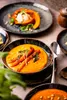 A close-up shot of a bowl of soup with carrots and herbs, with other plates of food in the background. Náhľad obrázku produktu
