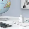 A white USB wall charger sits on a desk next to a smartphone and a globe. Anteprima dell’immagine prodotto