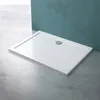 A white shower tray with a silver drain is placed on a concrete floor in front of a teal wall. Produktbild-Vorschau