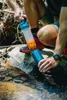 A person is filtering water from a stream into a blue container using a water filter bottle. Anteprima dell’immagine prodotto