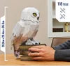 A person's hands are resting on a stack of books next to a 3D model of Hedwig the owl from Harry Potter. Produktbild-Vorschau