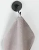 A black wall hook is mounted on a white wall, holding a gray towel. Produktbild-Vorschau