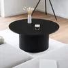 A round black coffee table with a fluted base, a vase with dried flowers, and a glass of coffee on it, placed on a rug in a living room. Voir les images du produit