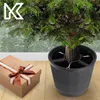 A Christmas tree stand with a gift box next to it, set on a wooden floor with a patterned wallpaper in the background. Voir les images du produit