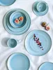 A collection of blue ceramic plates and cups arranged on a white cloth. Produktbild-Vorschau